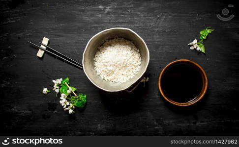 Rice in an old pot and soy sauce. On a black wooden background.. Rice in an old pot and soy sauce.