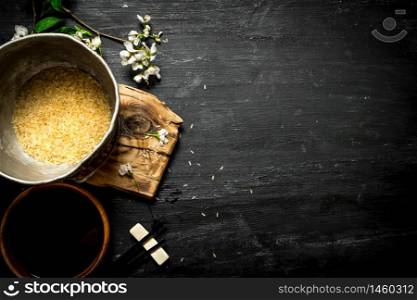 Rice in an old pot and soy sauce. On a black wooden background.. Rice in an old pot and soy sauce.
