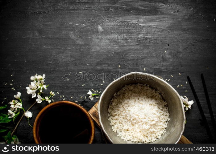 Rice in an old pot and soy sauce. On a black wooden background.. Rice in an old pot and soy sauce.