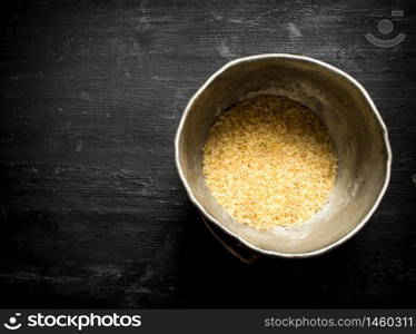 Rice in an old pot. On a black wooden background.. Rice in an old pot.