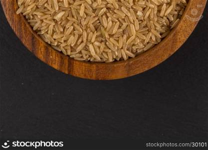 Rice in wooden bowl on dark stone background