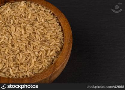 Rice in wooden bowl on dark stone background