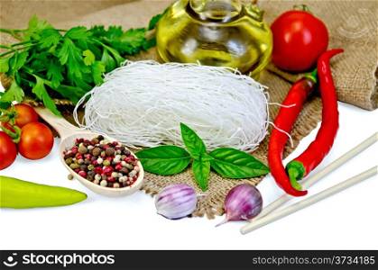 Rice noodles thin, tomatoes, different peppers, chopsticks, garlic, basil, oil, sacking isolated on white background