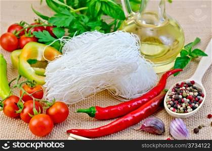 Rice noodles thin, tomatoes, peppers, chopsticks, garlic, basil, vegetable oil on a background of sack cloth