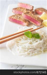 Rice noodles with fried tuna in sesame seeds on the white plate