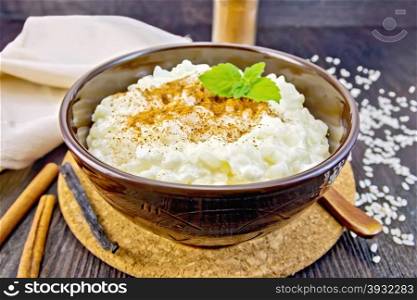 Rice porridge with cinnamon, mint in a brown bowl, napkin, cinnamon sticks, spoon the vanilla pod on a dark wooden board