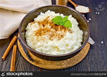 Rice porridge with cinnamon, mint in a brown bowl, napkin, cinnamon sticks, spoon the vanilla pod on a wooden board