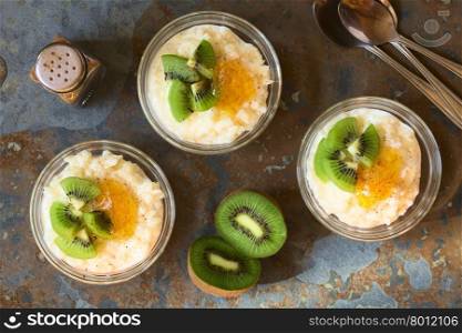 Rice pudding with kiwi pieces, orange jam and cinnamon in small glass bowls, photographed overhead on slate with natural light