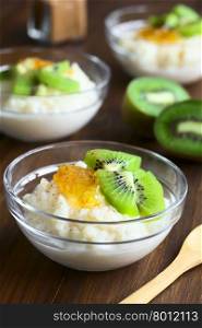 Rice pudding with kiwi pieces, orange jam and cinnamon in small glass bowls, photographed on dark wood with natural light (Selective Focus, Focus on the kiwi piece in the front)