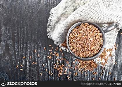 Rice red raw in a clay cup on burlap on the background of wooden board from above