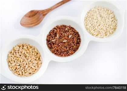 rice , red rice , wheat grains on white bowl and wooden spoon