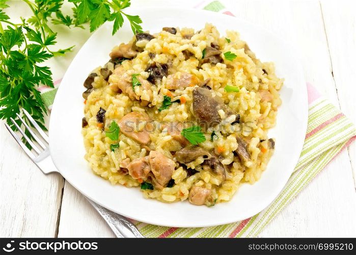 Rice risotto with mushrooms, chicken meat, cheese and garlic in a plate on a kitchen towel, fork, parsley on a wooden board background
