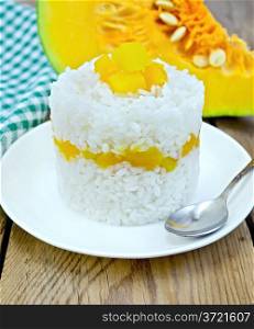 Rice with boiled pumpkin and spoon on white plate, raw sliced pumpkin, green cloth on a background of wooden boards