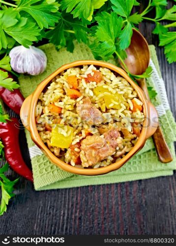 Rice with chicken, tomatoes, carrots, zucchini and garlic in a bowl on a napkin, spoon, parsley on a background of wooden boards on top