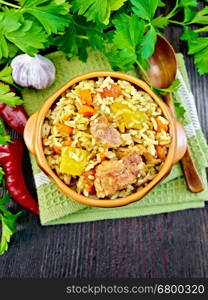 Rice with chicken, tomatoes, carrots, zucchini and garlic in a bowl on a napkin, spoon, parsley on a background of wooden boards on top
