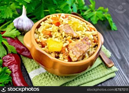 Rice with chicken, tomatoes, carrots, zucchini and garlic in a clay bowl on a napkin, spoon, parsley on a wooden boards background
