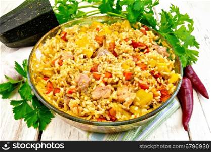 Rice with chicken, tomatoes, carrots, zucchini and garlic in a glass pan on a napkin, parsley on a wooden boards background