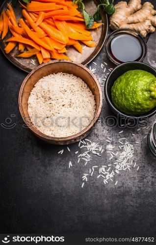Rice with chopped vegetables, lime, ginger and soy sauce on dark rustic background, top view, border. Asian cuisine concept