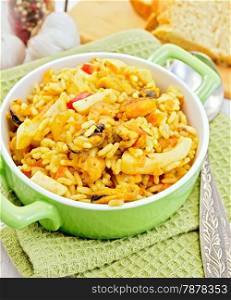 Rice with seafood and saffron in a green pot on a napkin, spoon, garlic bread on a wooden boards background