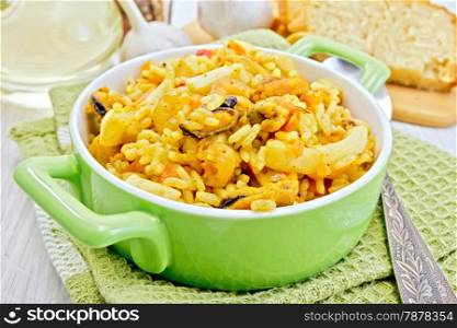 Rice with seafood and saffron in a green pot on a napkin, spoon, garlic bread on the background light wooden boards