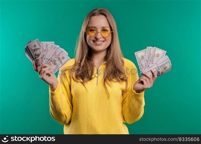 Rich excited blonde woman with cash money - USD currency dollars banknotes fan on blue wall. Symbol of jackpot, gain, victory, winning lottery. High quality. Rich excited blonde woman with cash money USD currency dollars banknotes on teal