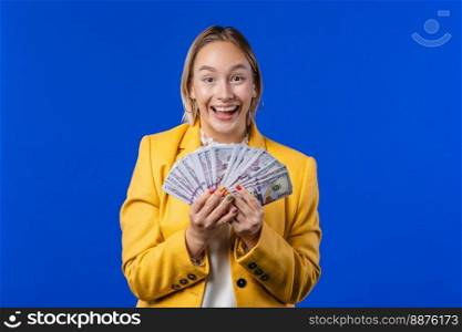 Rich excited blonde woman with cash money - USD currency dollars banknotes on blue wall. Symbol of jackpot, gain, victory, winning the lottery. High quality photo. Rich excited blonde woman with cash money - USD currency dollars banknotes