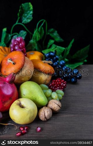 Rich harvest of various fruits and vegetables: decorative pumpkins, squash, apples, pears, pomegranates and grapes on the dark wooden background