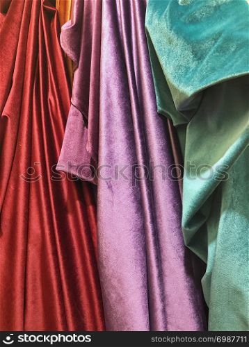 Rich red, purple and green bolts of fabric are draped from a rack in a cloth store in the souk of Marrakesh in Morocco.