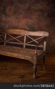 Rich, weathered wooden bench shot in the studio against a rich brown background on a wood floor. Plenty of copy space.