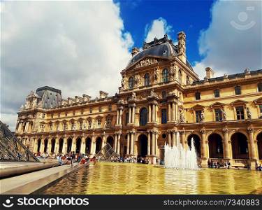 Richelieu wing of the Louvre building with fountain, tourists and the glass Pyramid in Paris, France.