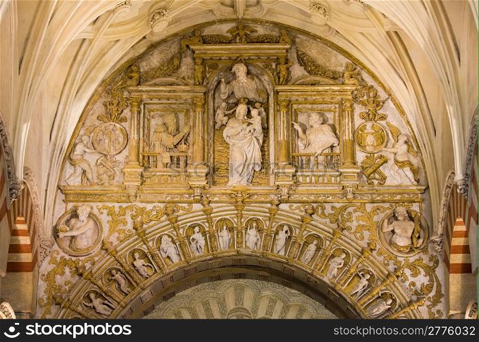 Richly decorated ornate space between two arches with religious reliefs inside the Mezquita Cathedral in Cordoba, Andalusia, Spain.