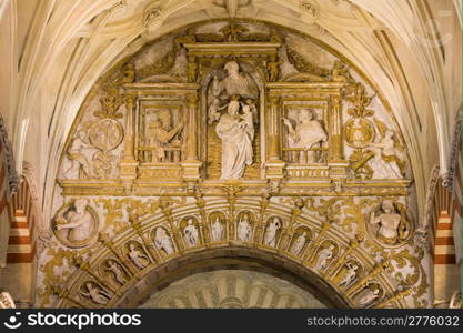 Richly decorated ornate space between two arches with religious reliefs inside the Mezquita Cathedral in Cordoba, Andalusia, Spain.