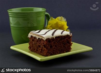 Richly delicious red velvet cake on contemporary green, square plate with classic mug and yellow flower behind. All on dark background with copy space on right.