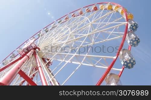 Ride on ferris wheel in amusement park. Colorful ferris wheel over the blue sky on sunny day. View from the bottom to the top.