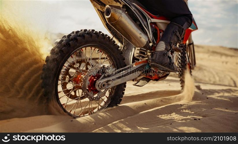 Rider driving in motocross race. Focus on skid rear wheel. Biker in ground track with dusty trail. Rider driving in motocross race skid wheel