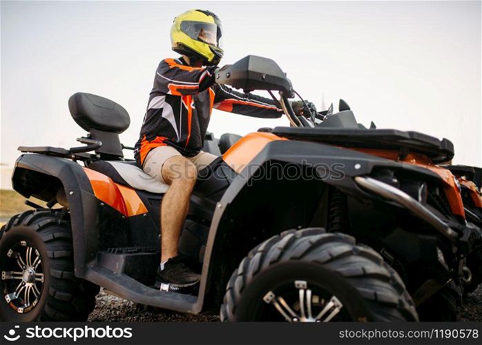 Rider in helmet and equipment on quad bike, front view, closeup. Male quadbike driver, atv riding. Rider in helmet on quad bike, front view, closeup