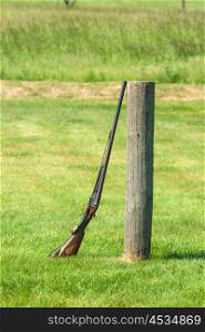 Rifle standing against a wooden pole on a green meadow