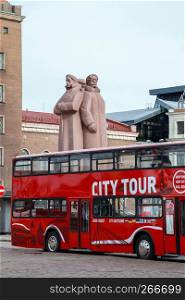 Riga sightseeing bus tour on the Latvian Riflemen Square Latvia. Latvian Riflemen monument behind the tourist bus. Riga city view with tourist bus. Tourist bus in downtown Riga.