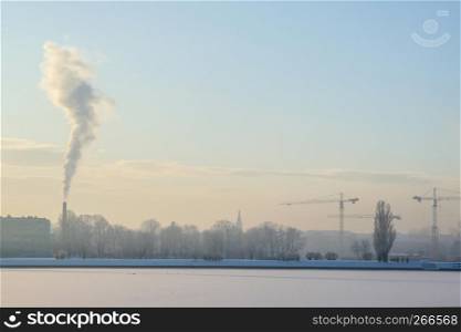 Riga view in winter; Riga, capital city of Latvia in winter time. View of Riga with frozen river Daugava and smoky chimney. City Riga with background of blue sky.