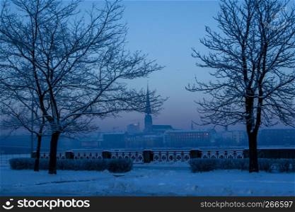 Riga view in winter; Riga, capital city of Latvia in winter time. View of St Peter's Church in winter. View of Old Riga with frozen river Daugava in the foreground. City Riga with background of blue sky.