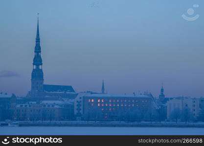 Riga view in winter; Riga, capital city of Latvia in winter time. View of St Peter's Church in winter. View of Old Riga with frozen river Daugava in the foreground. City Riga with background of blue sky.