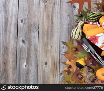 Right side border of autumn dinner setting with real gourd decorations, leaves and acorns on top of rustic wood