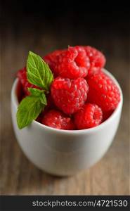 ripe and fresh raspberry in white cup on wooden table