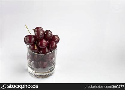 Ripe and red cherries are arranged in a clear glass on a light background, a picture in a high key. Red cherries in a clear glass on a light background