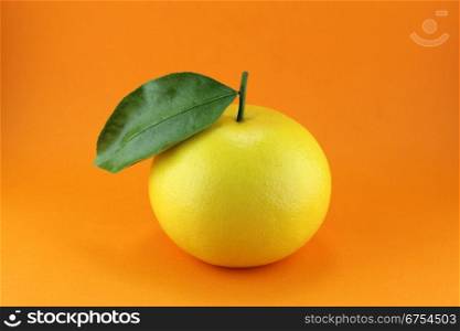 Ripe appetizing grapefruit with leaf on orange background.