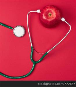 Ripe apple and green medical stethoscope on red background, health care concept
