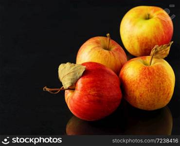 Ripe apples on a black background, close-up, space for text. Autumn harvesting. Reflection of apples on the table