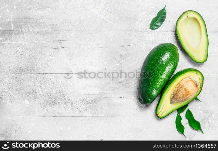 Ripe avocado with leaves. On white rustic background.. Ripe avocado with leaves.