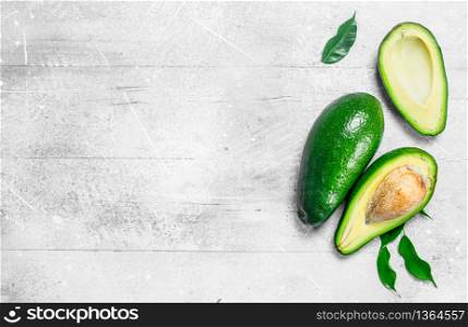 Ripe avocado with leaves. On white rustic background.. Ripe avocado with leaves.