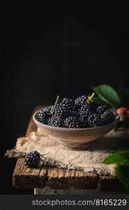 Ripe blackberries with leaves in a bowl on a dark rustic background. Ripe blackberries with leaves